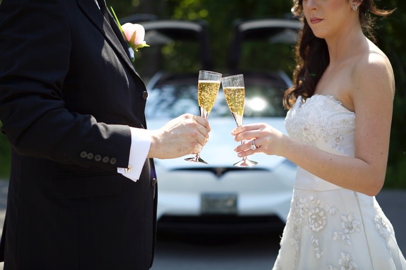 Couple holding champagne in front of a Tesla